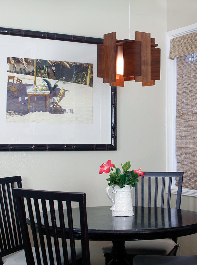 Abeo wooden pendant light hanging over a dining table with black chairs.