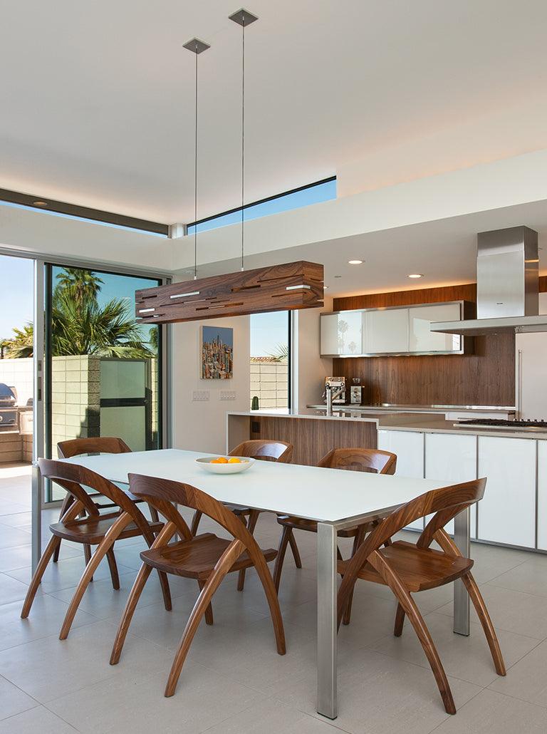 Aeris walnut linear pendant light hanging over a modern dining table with wooden chairs