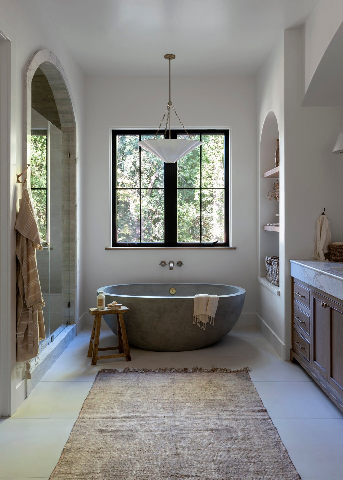 Alana pendant light with white scalloped shade and brass chains hanging over a concrete bathtub