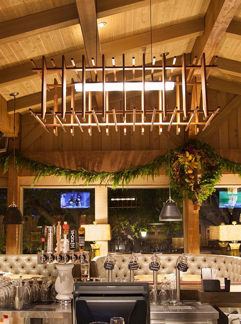 Arca linear pendant chandelier with walnut slats hanging over a bar counter.