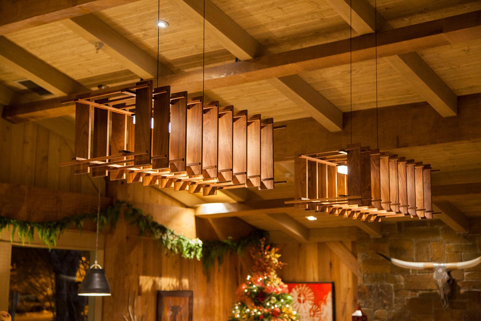 Arca linear pendant chandeliers with walnut wood slats hanging from a beamed ceiling