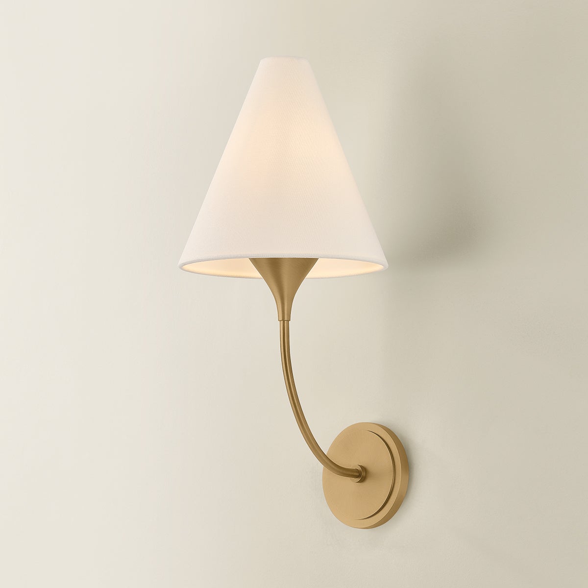Evermore brass wall sconce with a curved arm and a conical white linen shade.