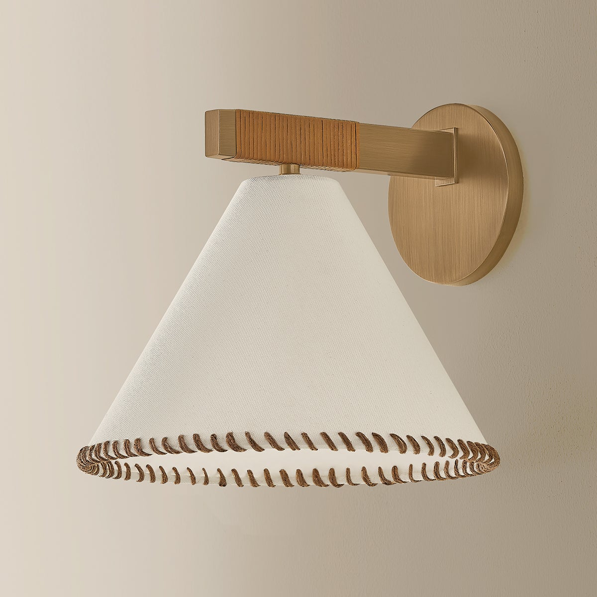 Stonely wall sconce with brass frame, jute wrap, and white linen shade with whip-stitching.