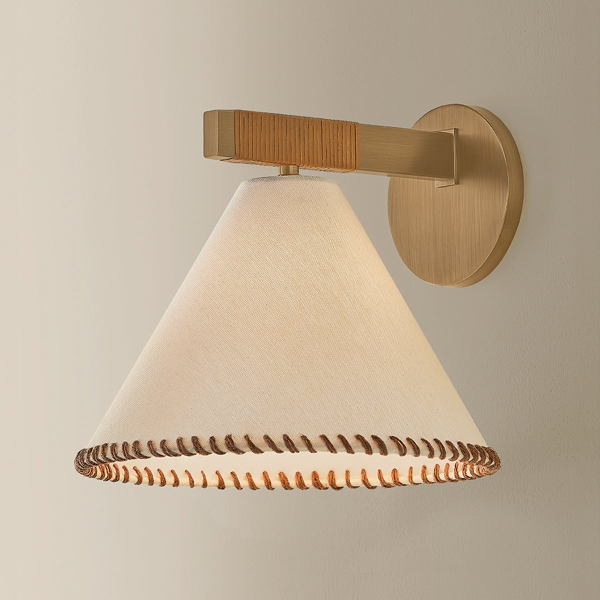 Stonely wall sconce with brass frame, jute wrap, and whip-stitched white linen shade.