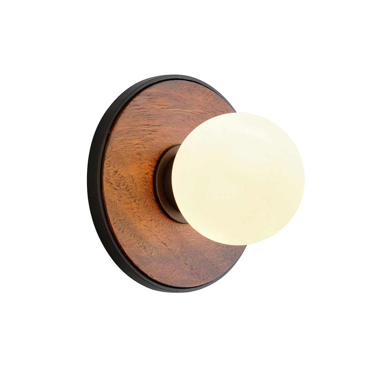 Cadet wall sconce with a round wood backplate, black metal trim, and a glowing white globe bulb.