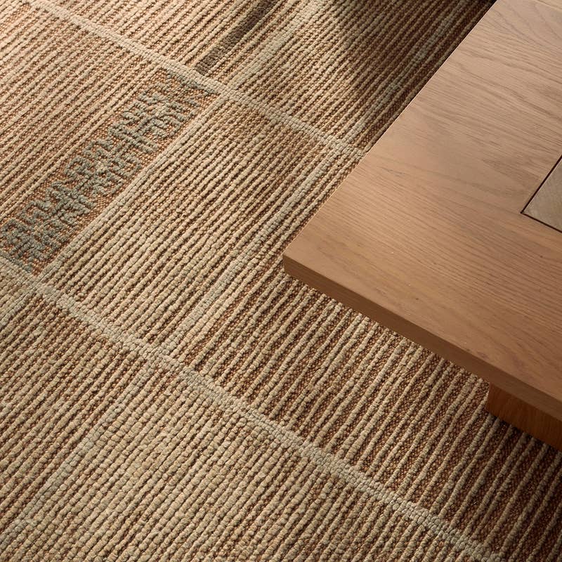 Bezem hand-knotted wool rug in warm beige and brown tones next to a wooden table.