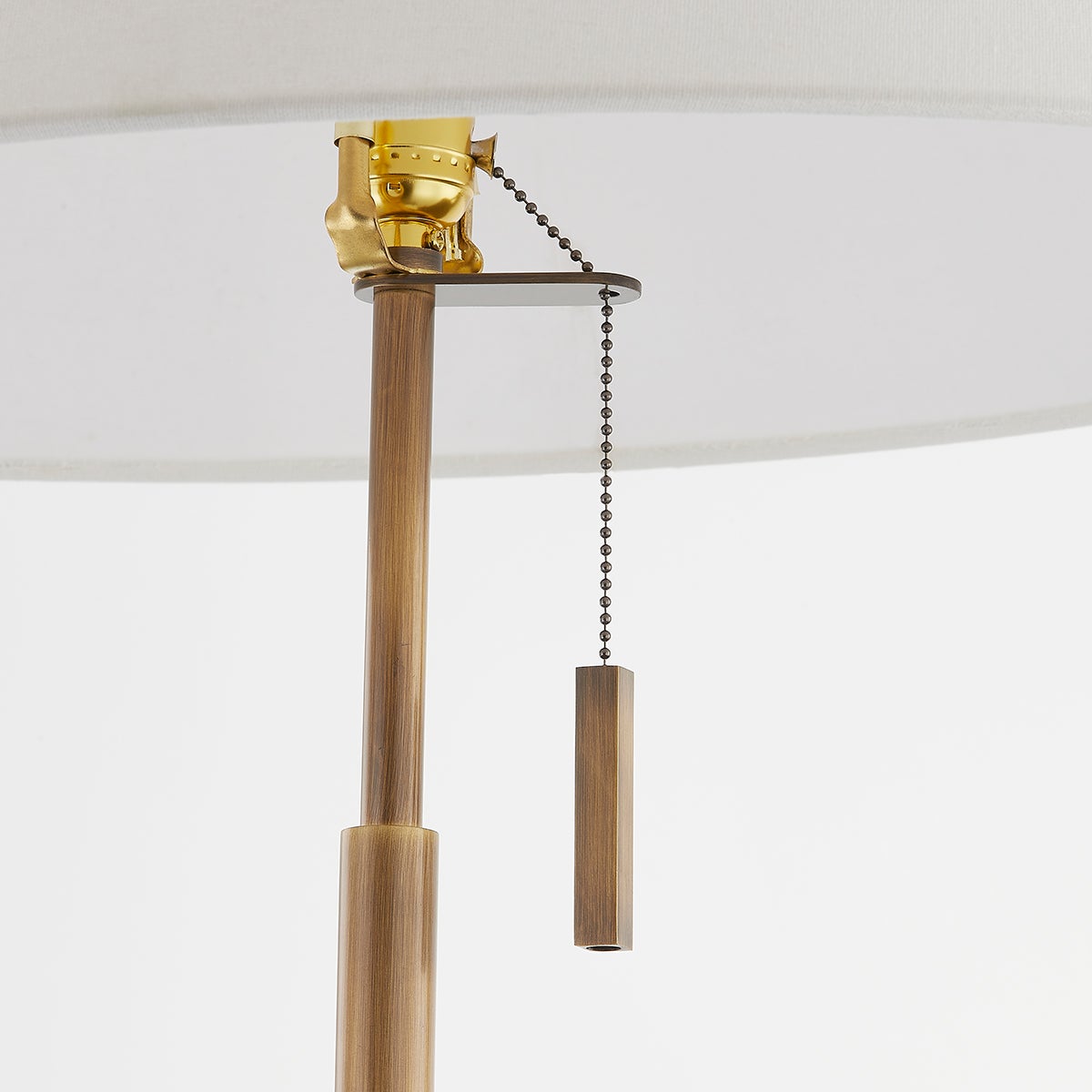 Clic floor lamp detail showing patina brass pole, pull chain switch, and off-white linen shade.