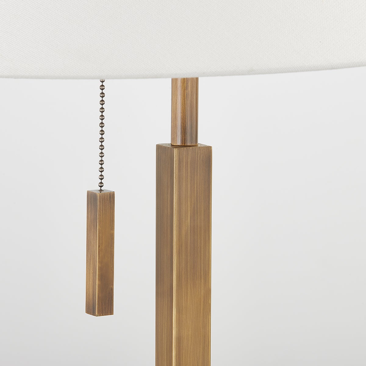 Clic table lamp in patina brass with a square body, pull chain, and off-white linen shade.