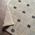 Cera Tiles hand-knotted wool rug with a geometric plaid pattern in muted grey, beige, and blue tones.