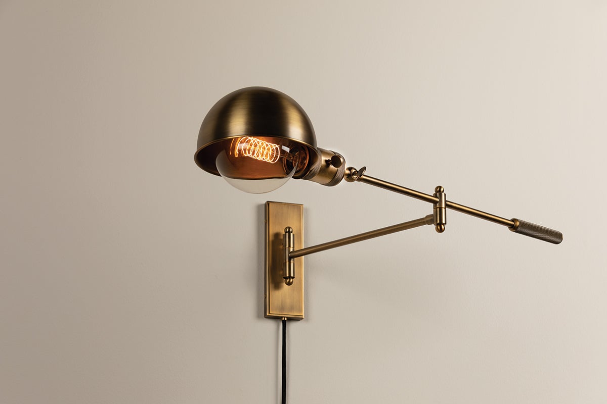 Cannon adjustable wall lamp in patina brass with a dome shade and exposed filament bulb.