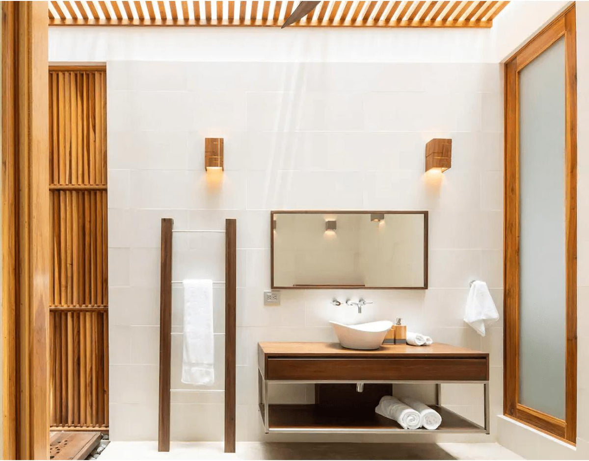 Two Claudo solid walnut wood sconces with warm LED light in a modern bathroom.