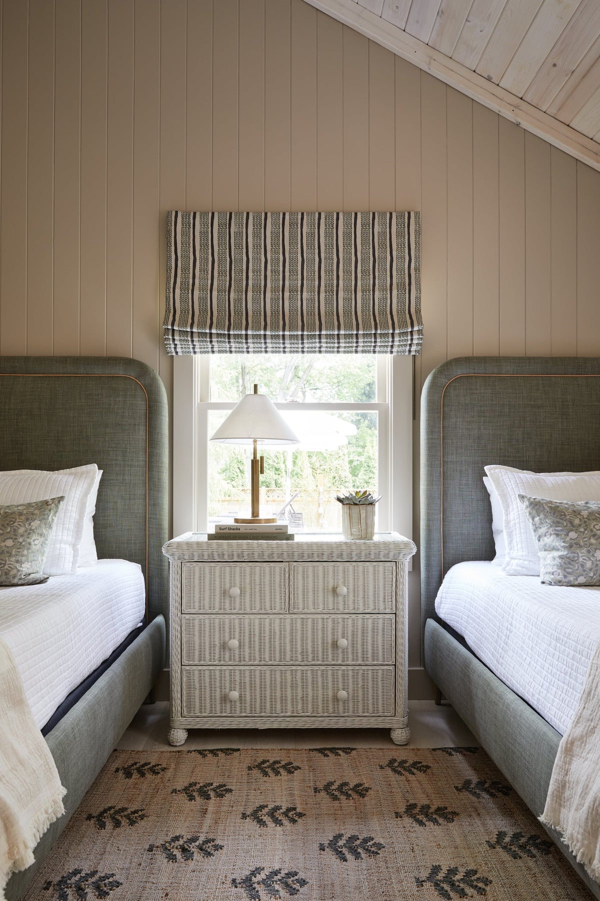 Clic brass table lamp with off-white shade on a wicker nightstand between two twin beds.