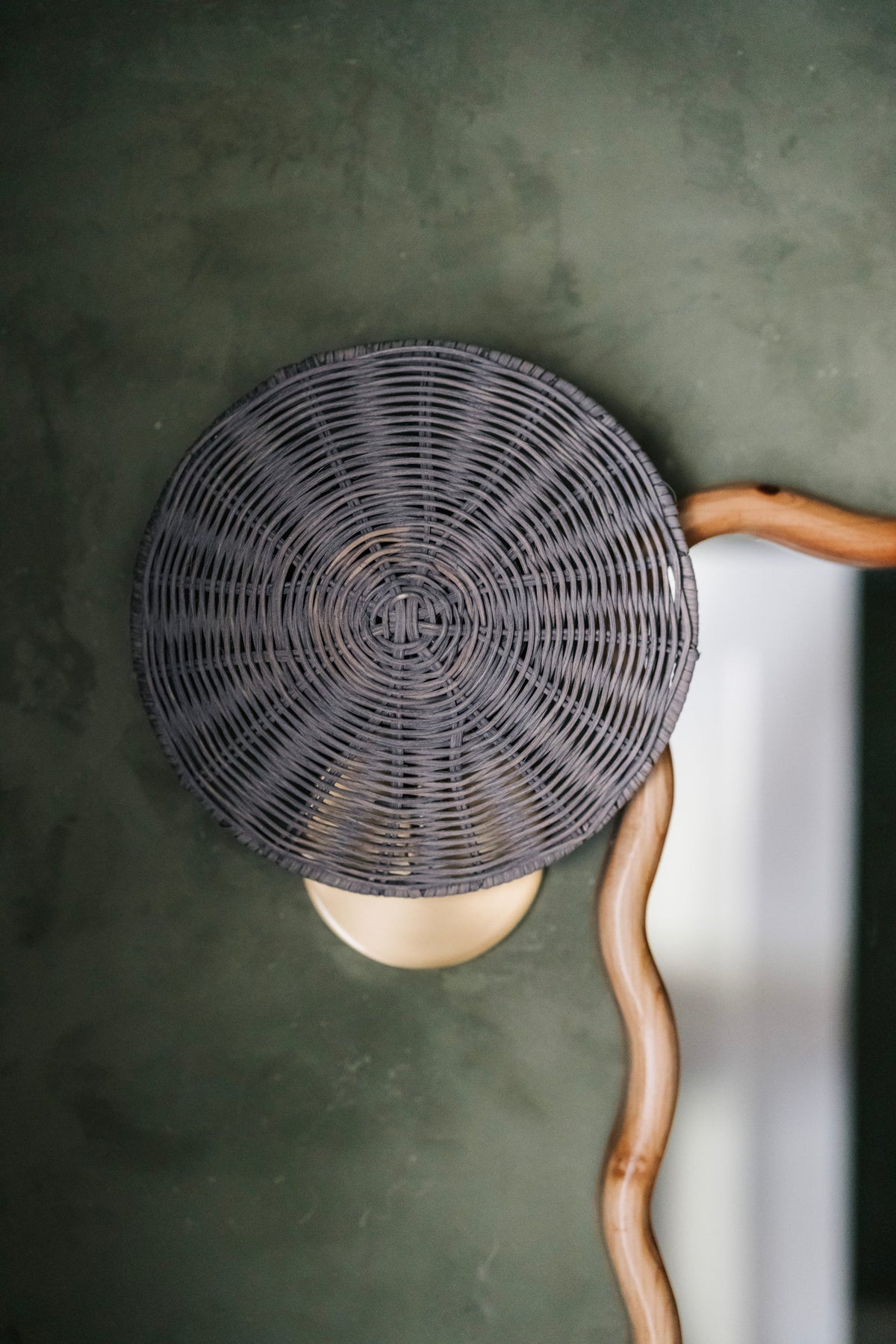 Destiny Wall Sconce with a round gray wicker shade and aged brass base on a green wall