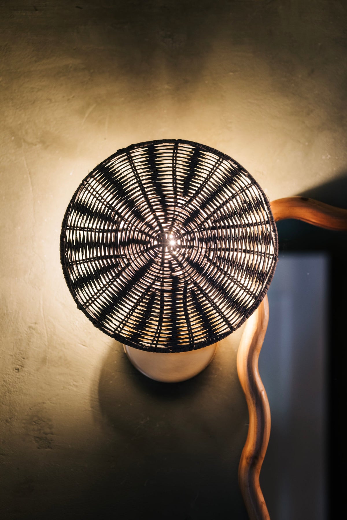 Destiny Wall Sconce with a round gray wicker shade emitting a warm golden glow on a wall.