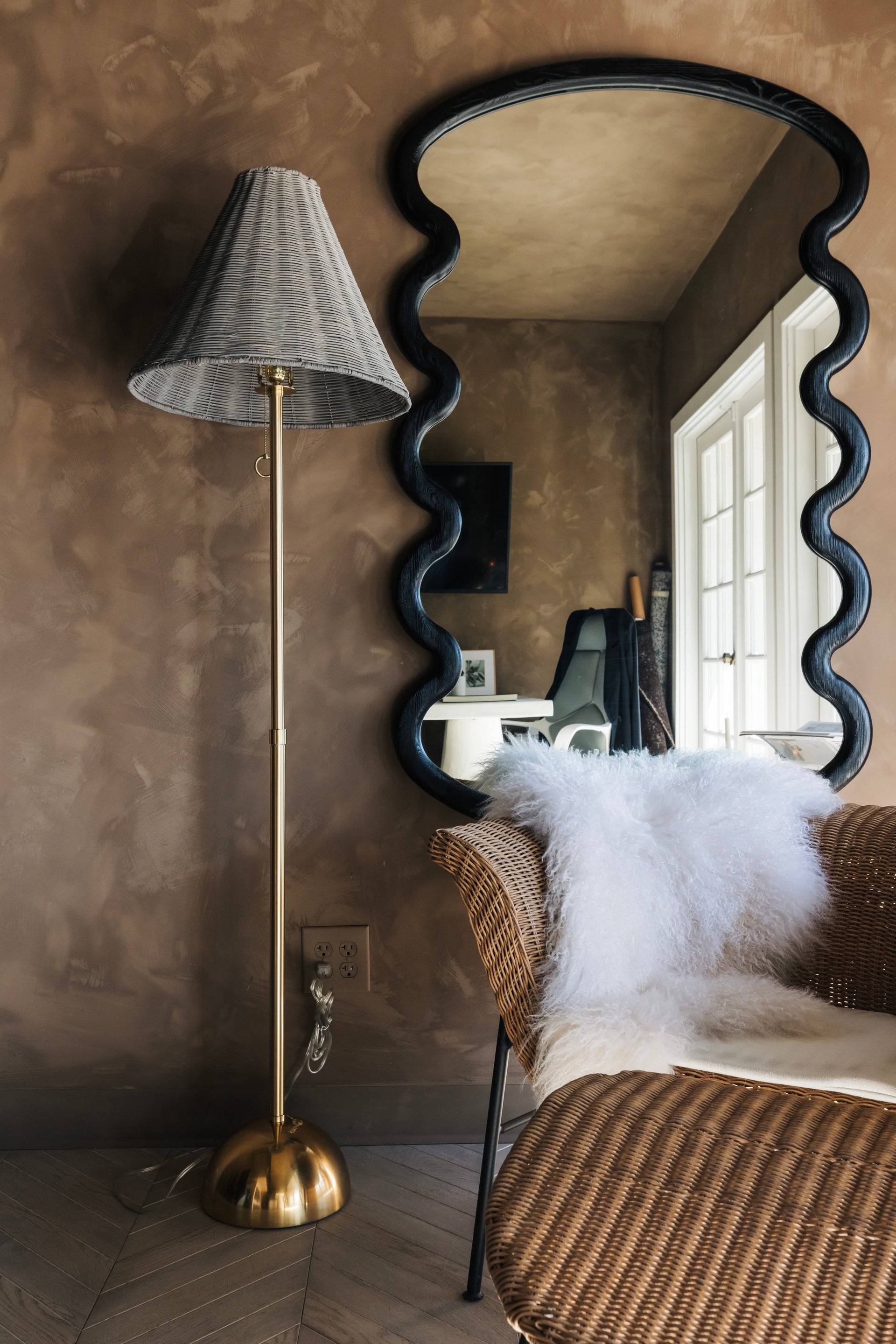 Destiny Floor Lamp with aged brass stand and gray wicker shade next to a wavy mirror.