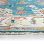 Everly hand-knotted wool rug with teal and cream traditional floral patterns and fringed edge.