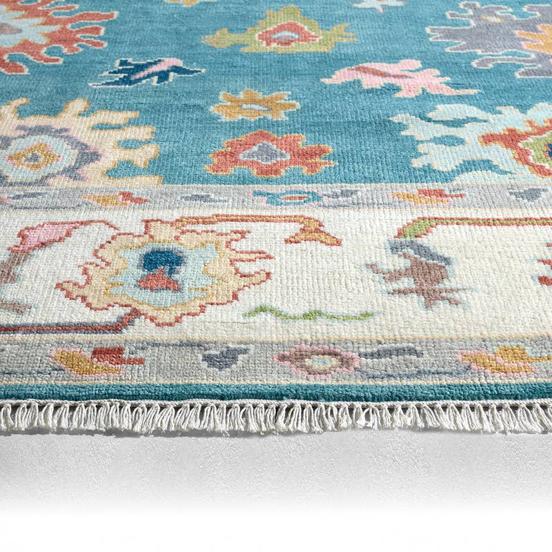 Everly hand-knotted wool rug with teal and cream traditional floral patterns and fringed edge.
