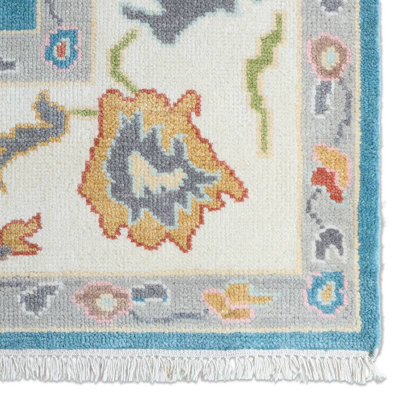 Everly hand-knotted wool rug corner with floral patterns, blue border, and white fringe.