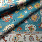 Everly hand-knotted wool rug in teal with colorful traditional patterns and a cream border.