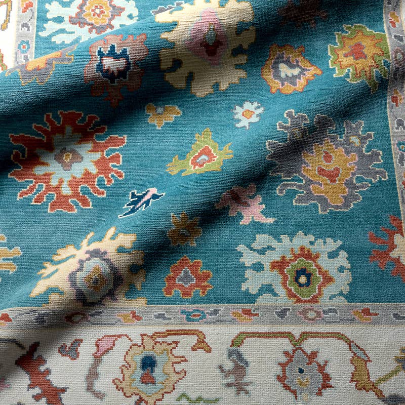 Everly hand-knotted wool rug in teal with colorful traditional patterns and a cream border.
