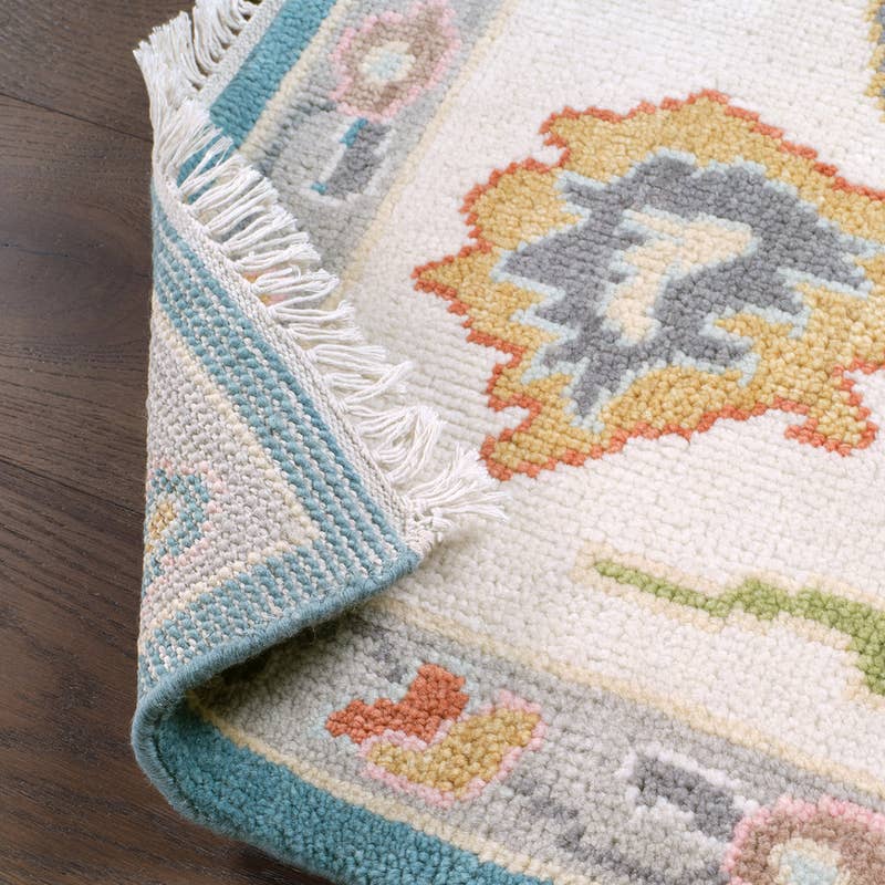 Everly hand-knotted wool rug with cream, blue, and gold traditional patterns and fringe.