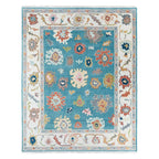 Everly hand-knotted wool rug featuring a teal center and white border with colorful floral motifs.