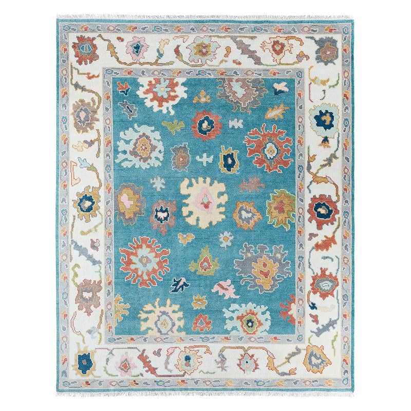 Everly hand-knotted wool rug featuring a teal center and white border with colorful floral motifs.