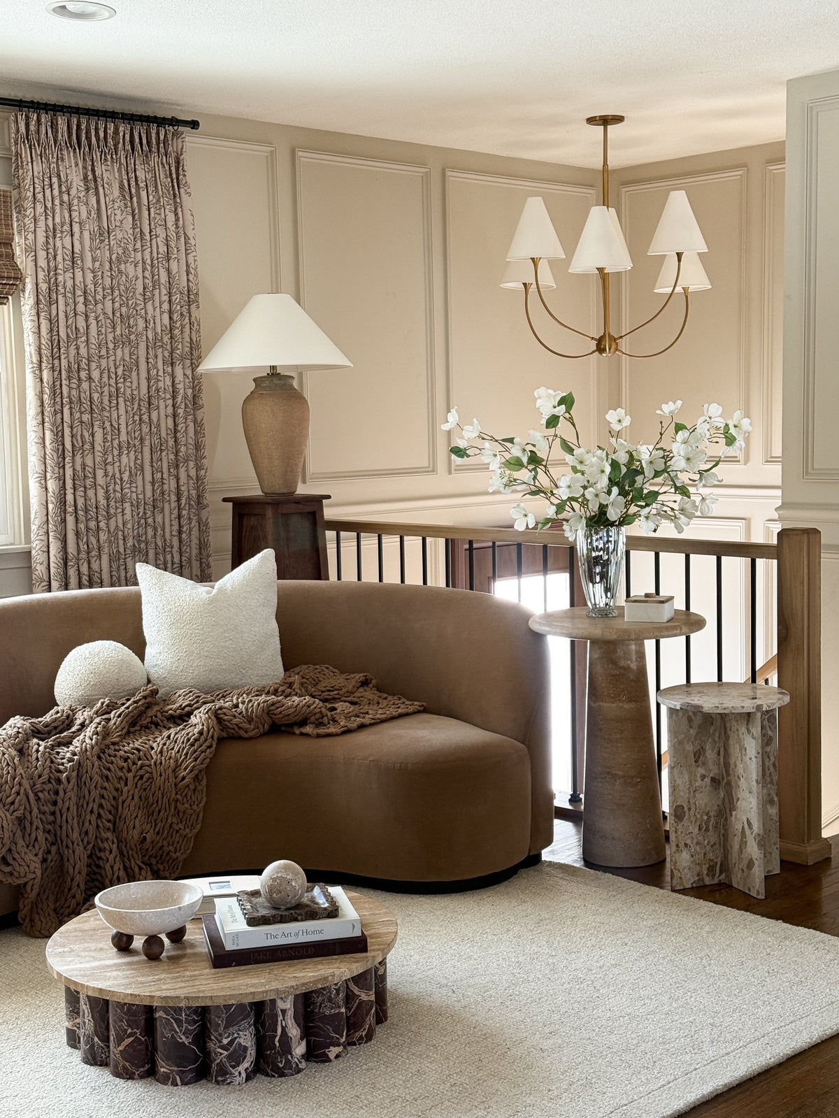 Evermore brass chandelier with white linen shades hanging in a warm, modern living room.