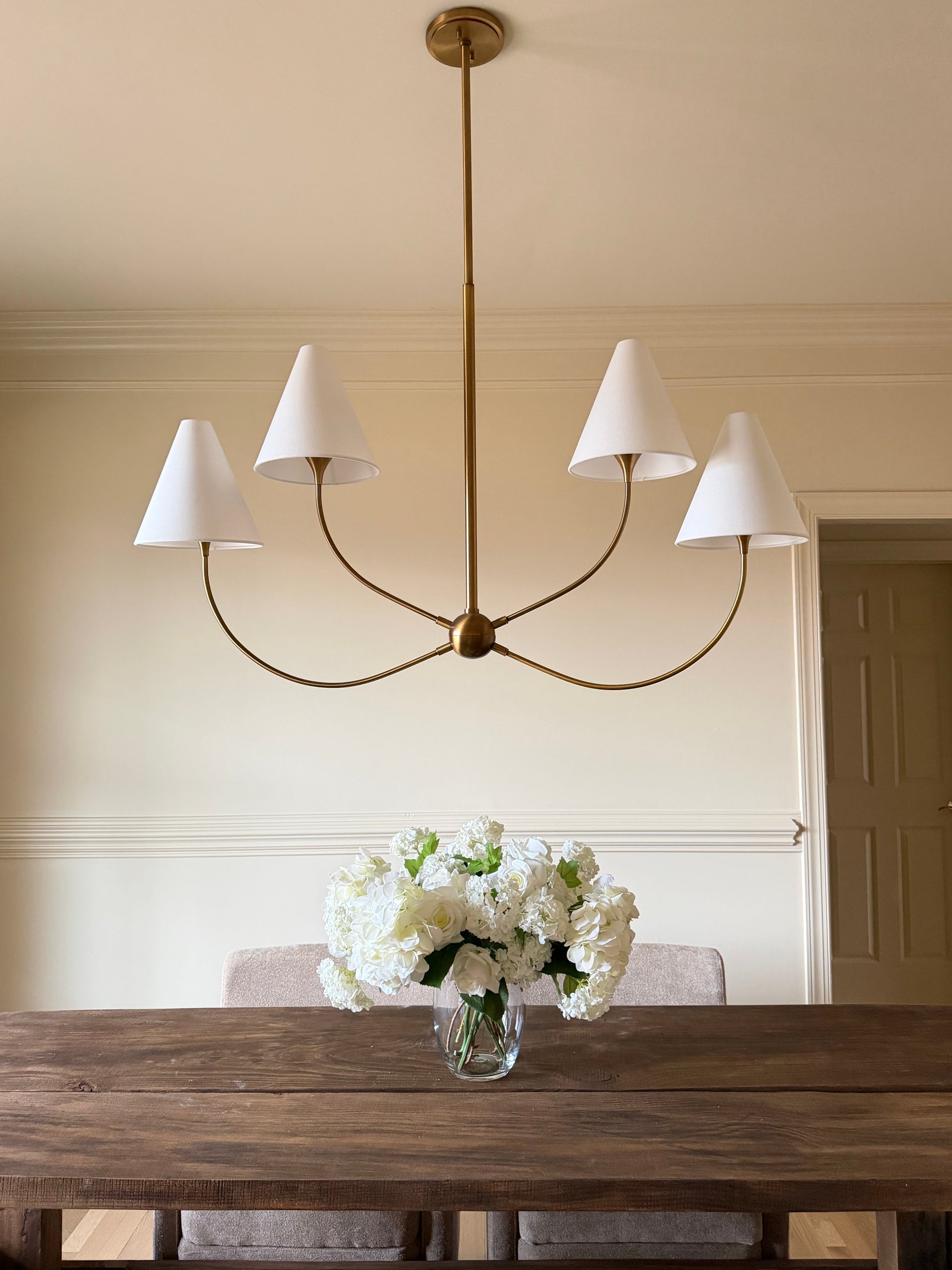 Evermore brass linear chandelier with four white linen shades over a dining table