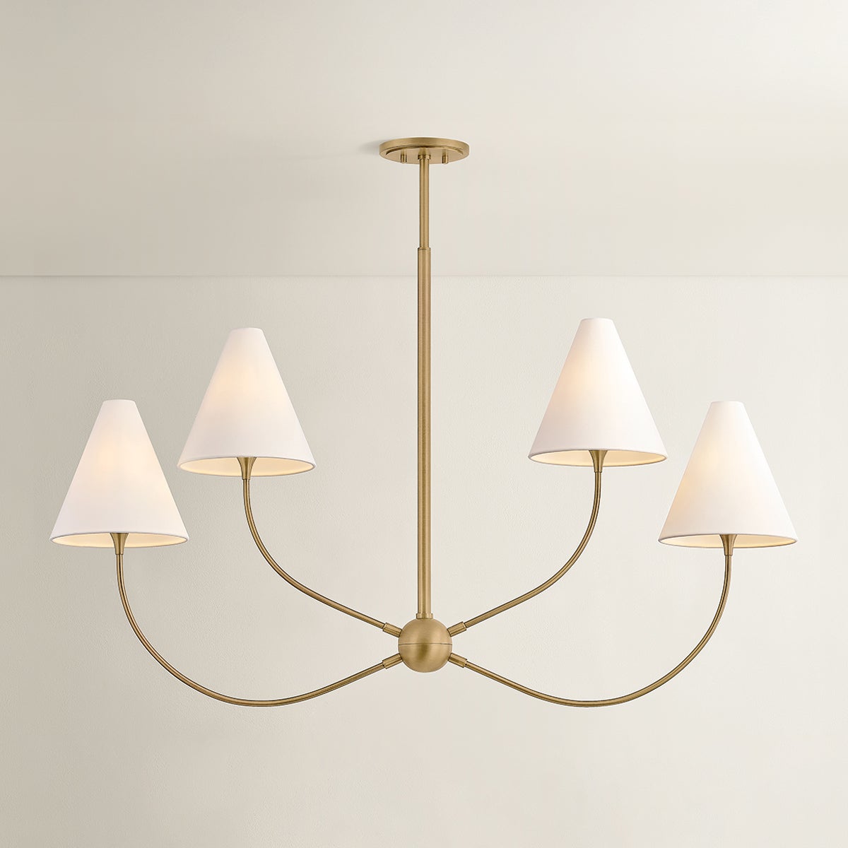 Evermore linear brass chandelier with four curved arms and off-white linen shades.