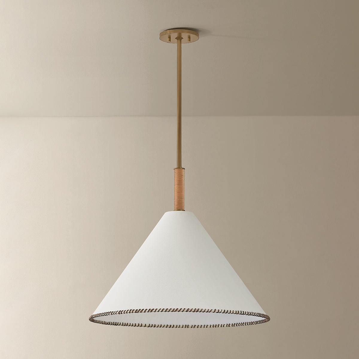 Stoney pendant light with a white conical linen shade, whip-stitched edge, and jute-wrapped brass stem.