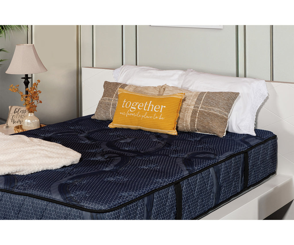 Siesta Mattress in dark blue quilted fabric with decorative pillows on a white bed frame.