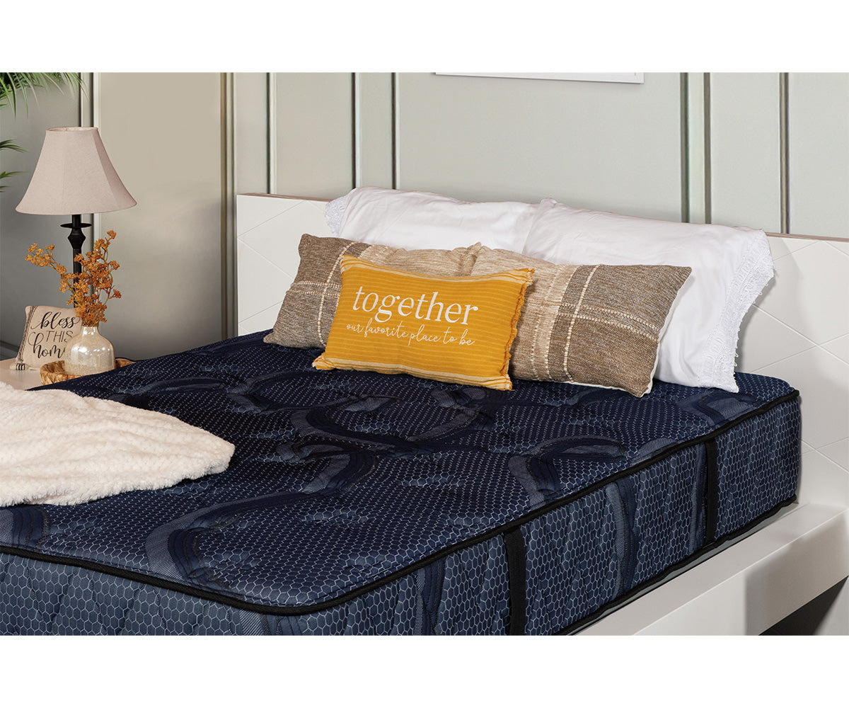 Siesta Mattress in dark blue quilted fabric with decorative pillows on a white bed frame.