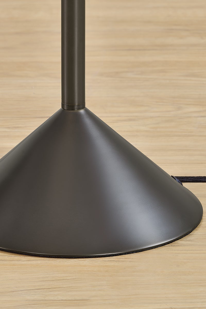 Conical dark metal base of the Harriet floor lamp on a light wood floor.