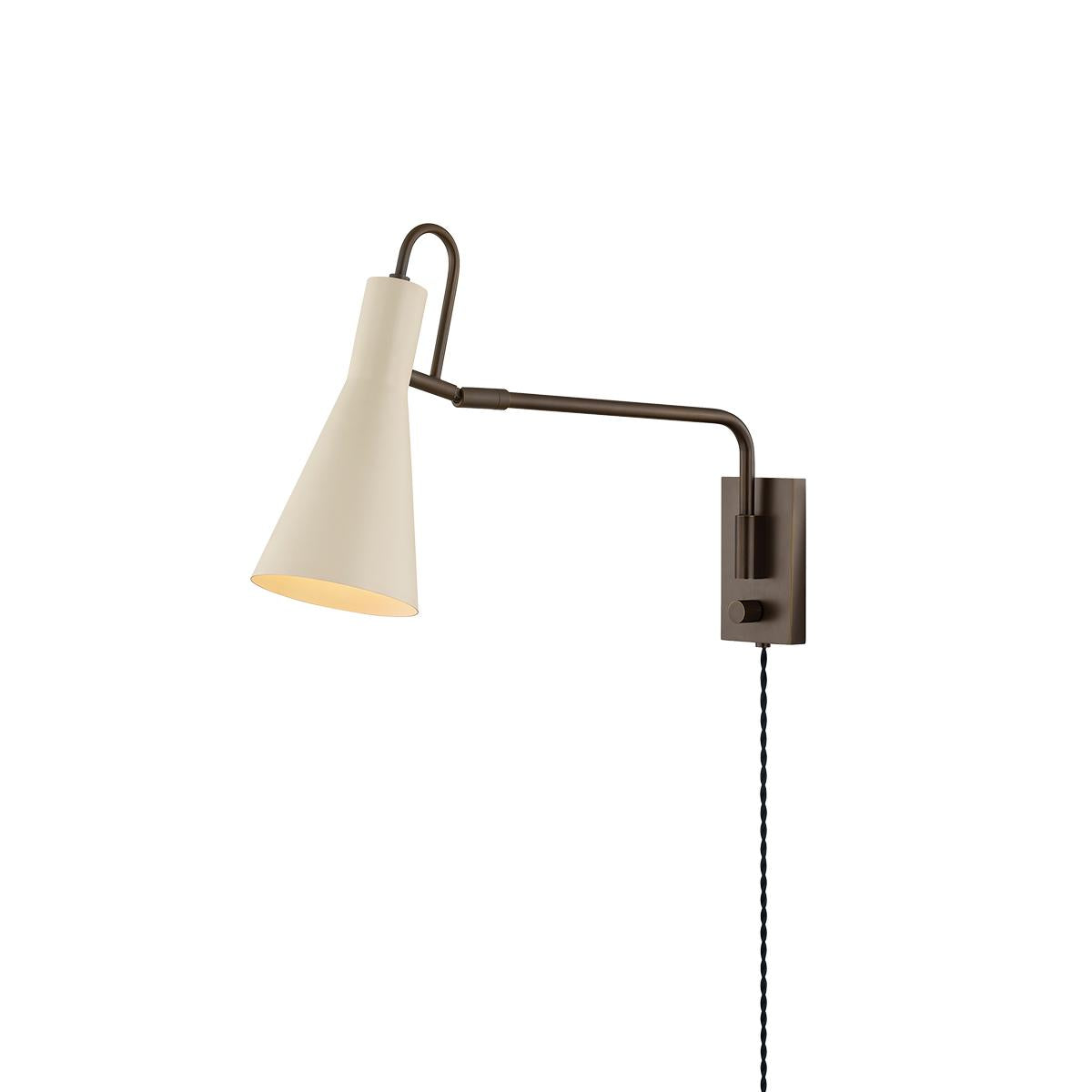 Yvette plug-in wall sconce with a soft bisque cone shade and adjustable dark metal arm.