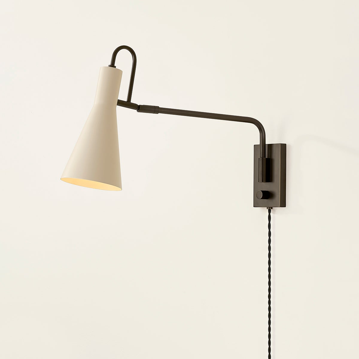 Yvette plug-in sconce with a soft bisque cone shade and adjustable dark metal arm.