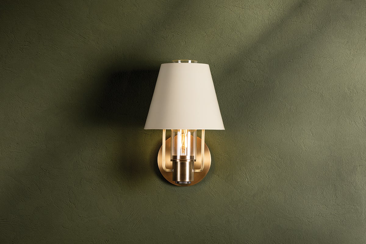 Kindle wall sconce with a tapered soft sand shade and patina brass metalwork on a green wall
