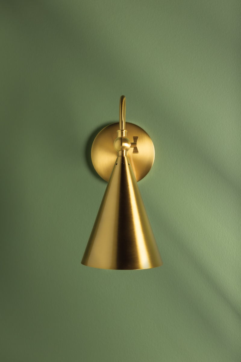 Lupe aged brass wall sconce with a cone shade and swivel key on a green wall