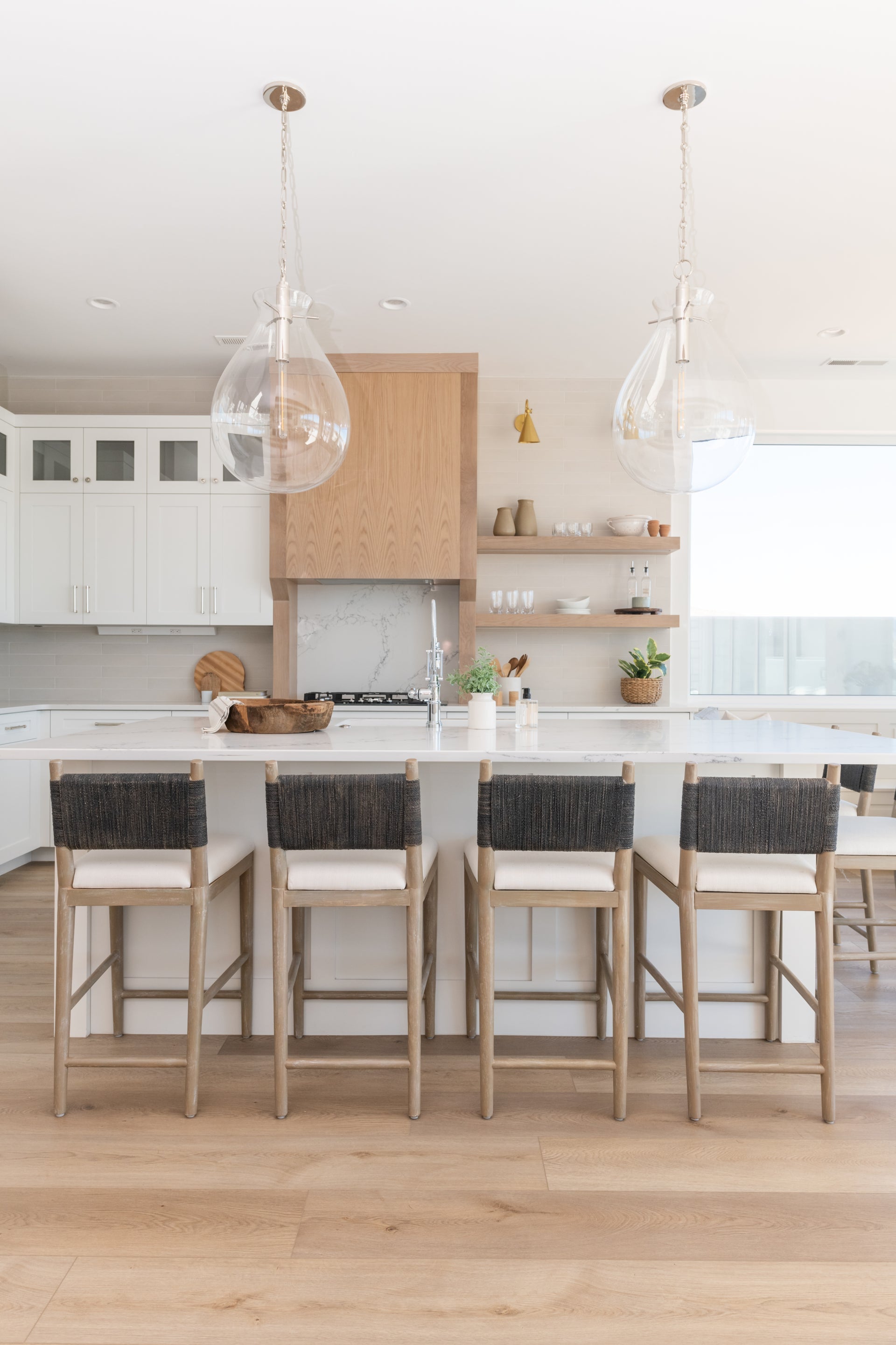 Lupe aged brass wall sconce mounted in a modern kitchen with glass pendant lights and island seating.