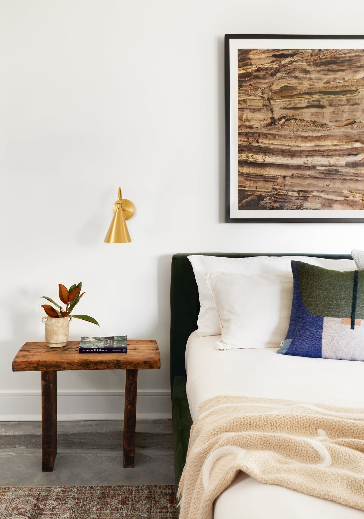 Lupe aged brass wall sconce mounted above a rustic wooden nightstand next to a bed.