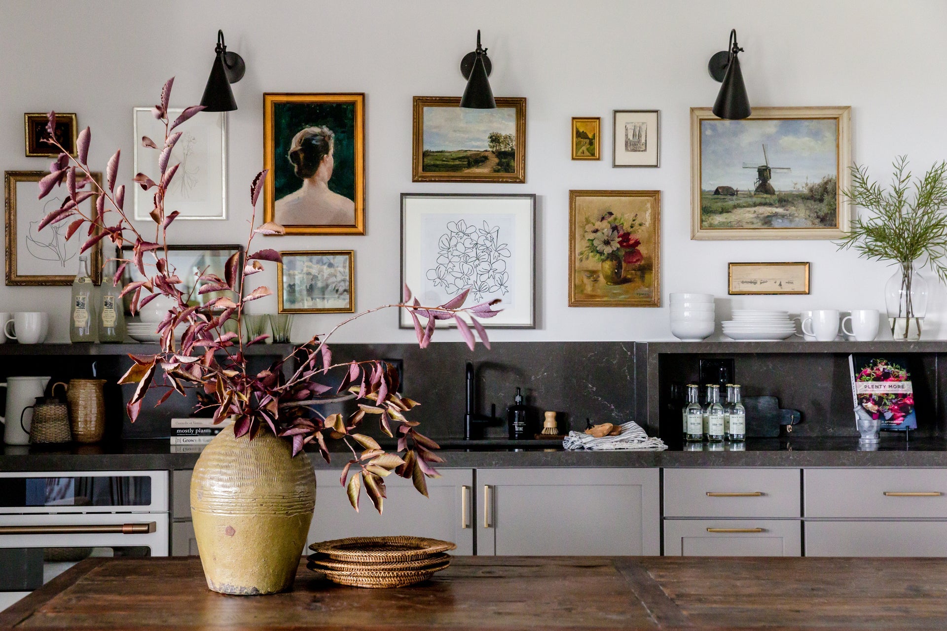 Three Lupe black cone wall sconces mounted above a gallery wall in a kitchen.