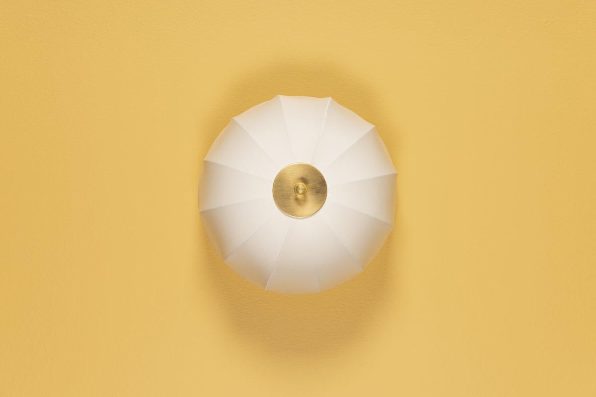 Meshelle white umbrella-shaped flush mount light with aged brass finial on a yellow background.