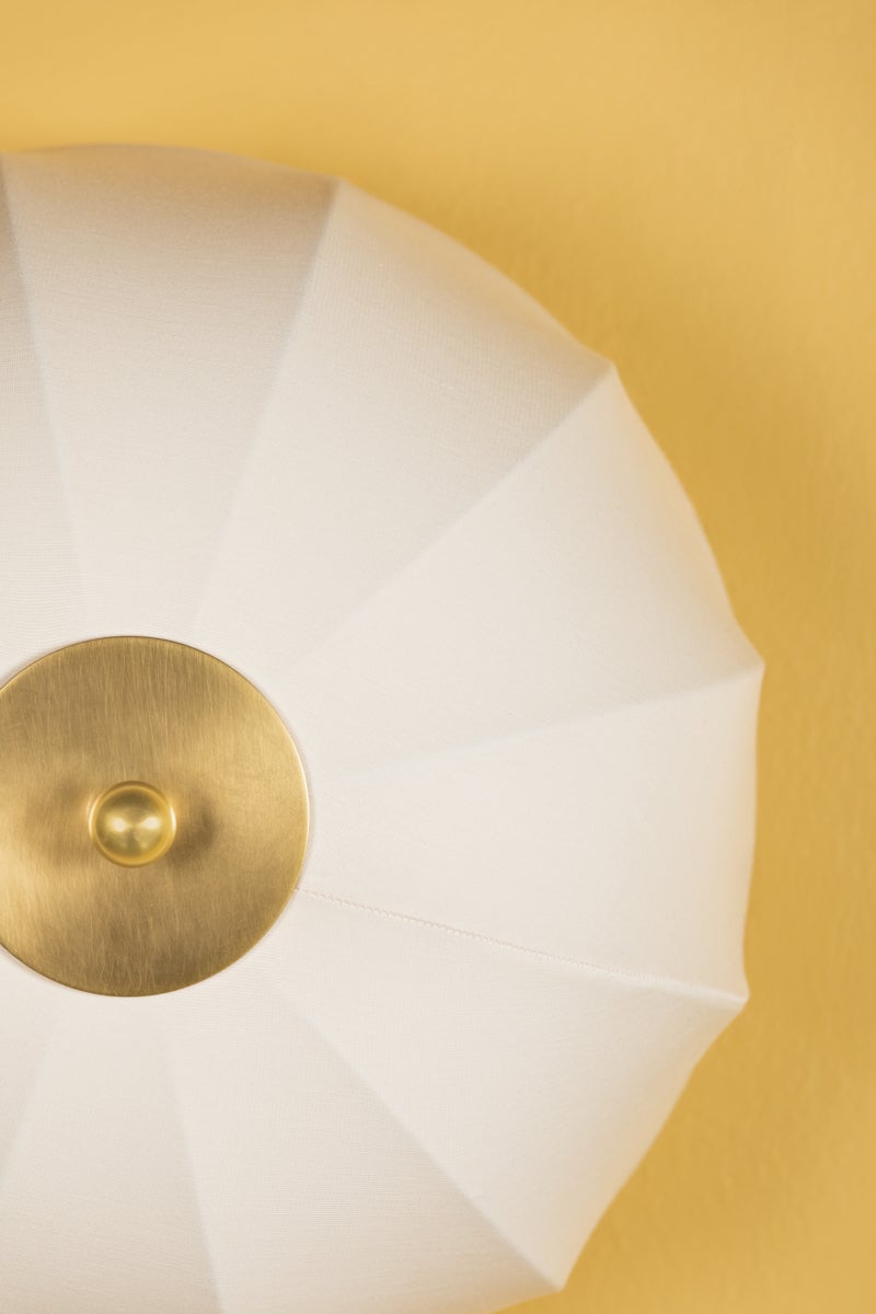 Meshelle white umbrella-shaped fabric flush mount light with aged brass finial on a yellow ceiling.