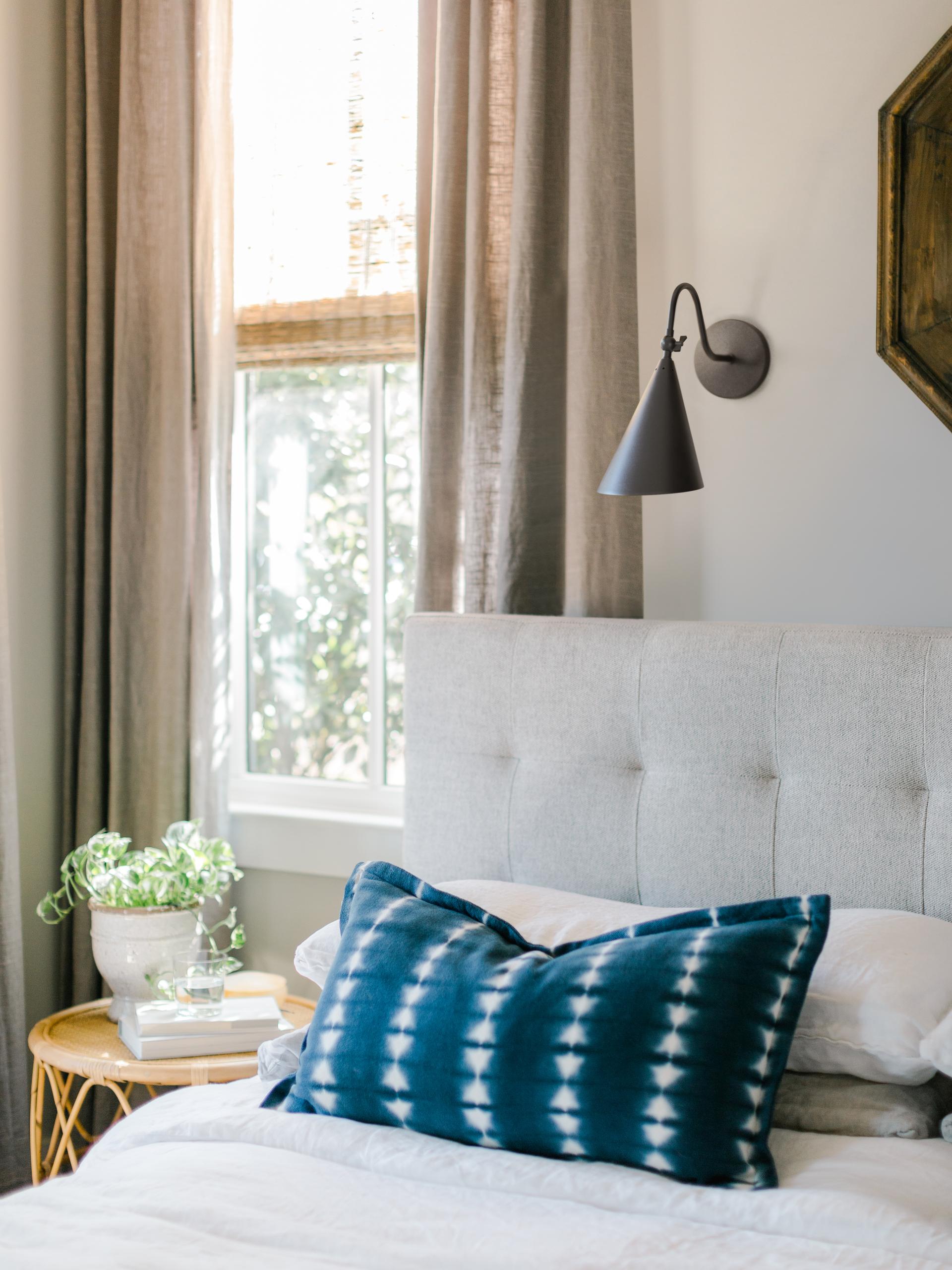 Lupe wall sconce in Old Bronze mounted above a bed with a tufted headboard.