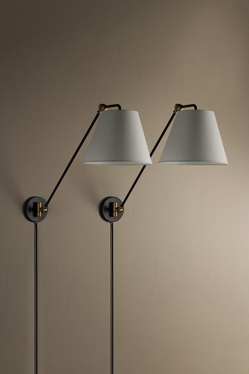 Two Navin plug-in sconces with black adjustable arms, brass accents, and white linen shades.