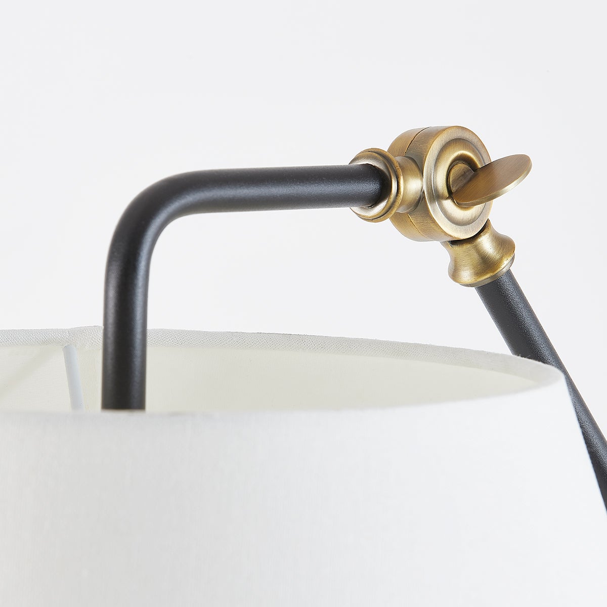Navin floor lamp detail showing textured black arm, patina brass adjustable joint, and white linen shade.