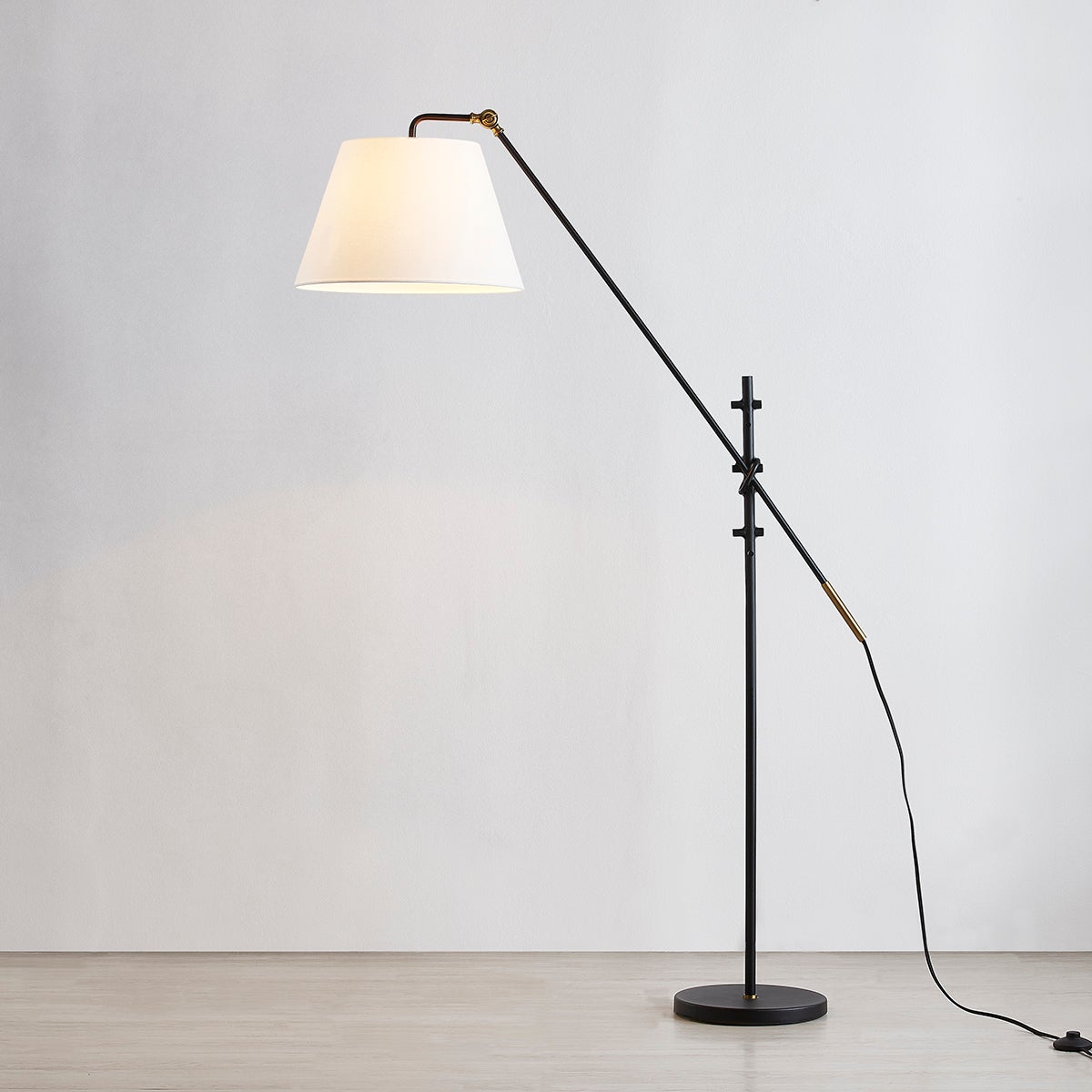 Navin floor lamp with textured black adjustable arm, patina brass accents, and white linen shade.