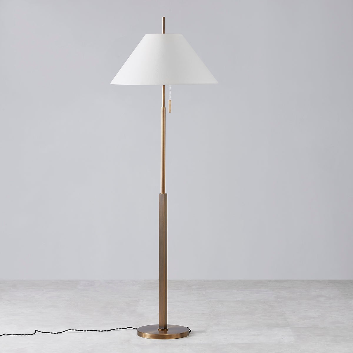 Clic floor lamp in patina brass with an off-white linen tapered shade and pull chain.