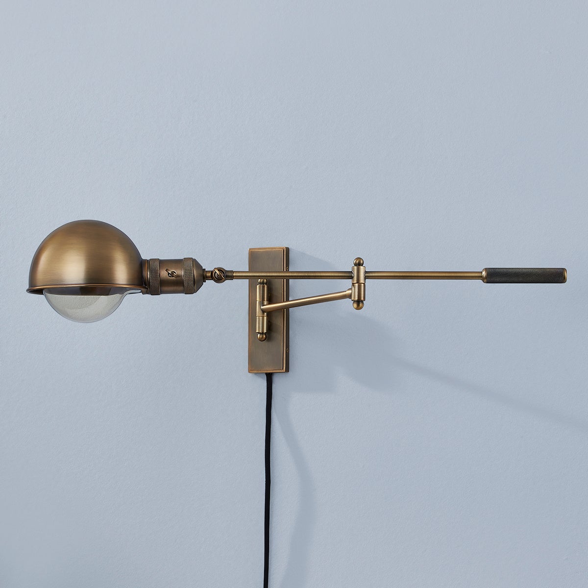 Cannon adjustable wall lamp in patina brass with a dome shade and swing arm.