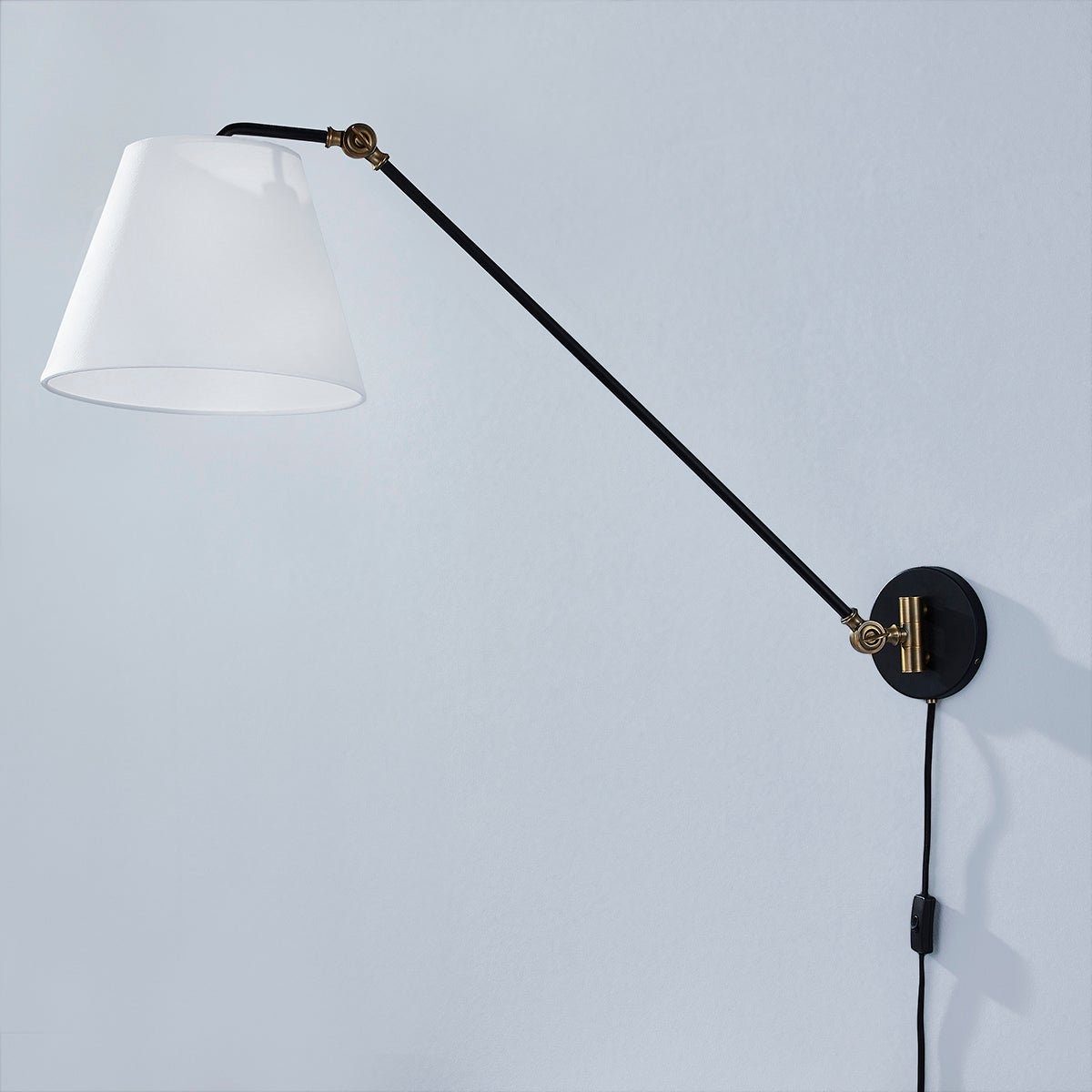 Navin plug-in sconce with black adjustable arm, brass accents, and white linen shade.